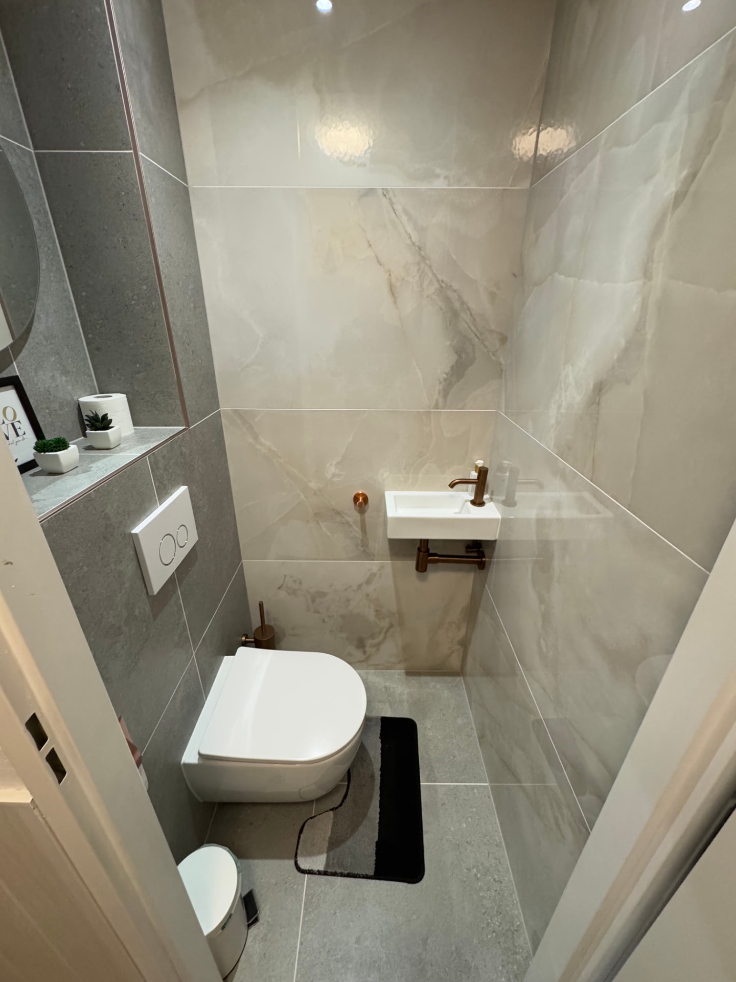 Gerenoveerd gastentoilet met marmerlook tegels en koperen kraan