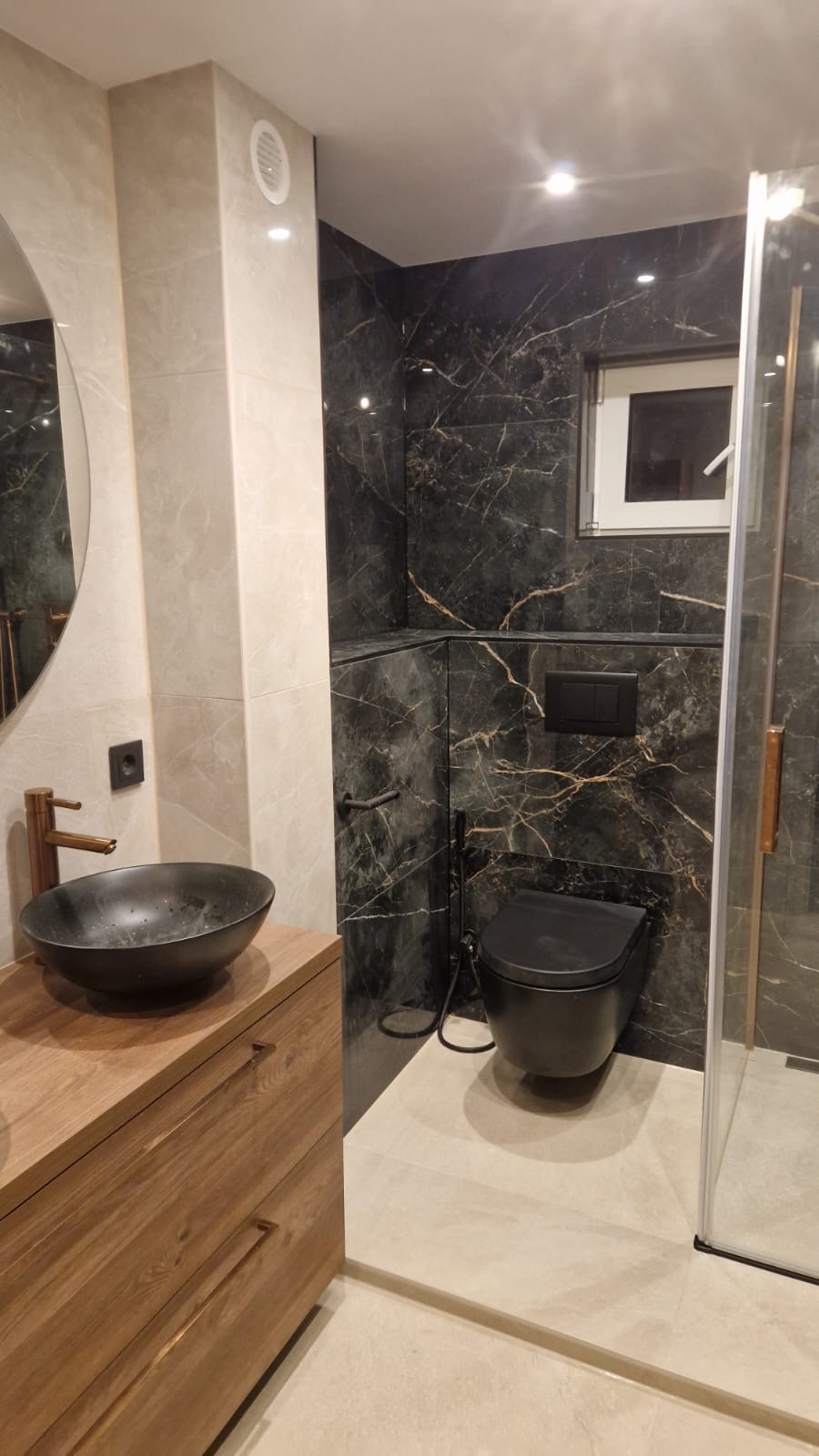 Badkamer met zwart marmer, houten meubel en koperen kranen